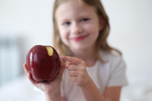 Beautiful little smiling girl eats red ripe apple. Benefits of apples for body concept