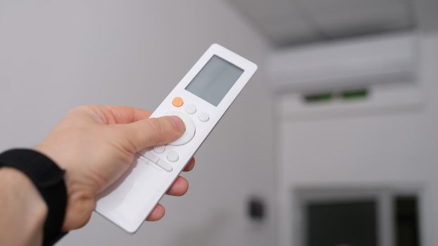 Hand with remote control is directed to air conditioner in room. Climate control indoor concept