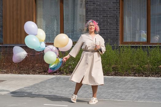 Woman in colored hair walks with an armful of balloons and drinks a refreshing beverage.