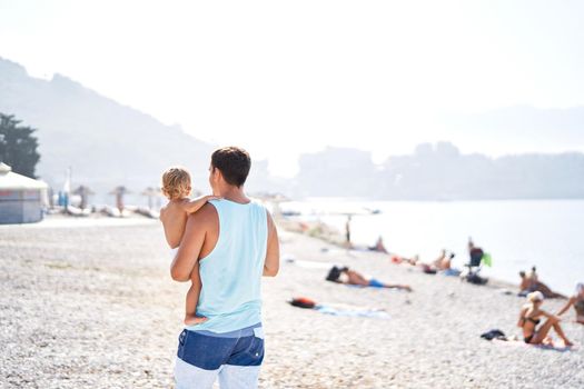 Dad with a little daughter in his arms walks on a pebble beach. High quality photo