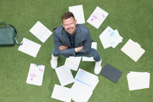Happy businessman scattered documents on green lawn, top view. Concept vacation, freedom from work, successful project