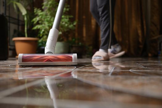 Cordless vacuum cleaner with turbo brush cleans tiles in living room. Modern home cleaning technology concept