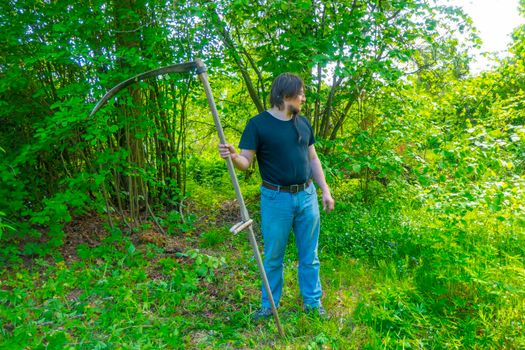 A man mows the grass with a hand scythe. Mow the grass with an old scythe. The farmer traditionally mows the lawn. The mower mows the green grass with a manual metal scythe.