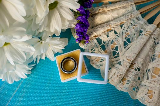 Wedding bouquet of bride. wedding card with original rings in a white box, a bouquet of white chrysanthemums or daisies and a white lace fan on a blue background