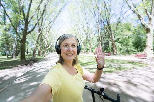 Active pensioner on a morning jog in the park, listening to music from headphones, looking at the phone camera and smiling, talking to friends via video link
