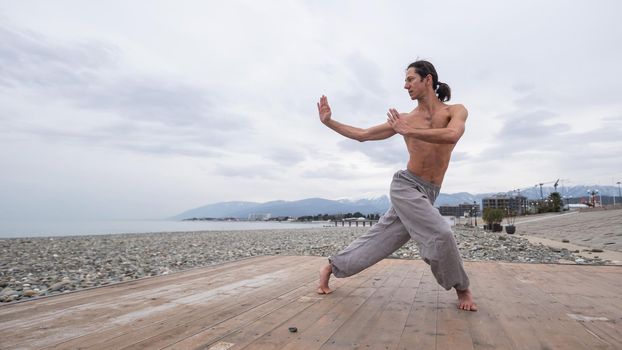 Caucasian man with naked torso practicing wushu on the seashore