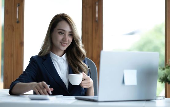 Beautiful young Asian businesswoman smiling holding a coffee mug and laptop working at the office..