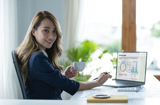 Smiling Asian businesswoman holding a coffee mug and laptop at the office. Looking at the camera..