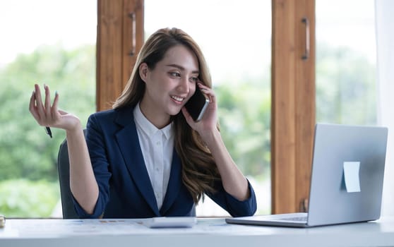 Beautiful young Asian businesswoman charming smiling and talking on the mobile phone in the office..