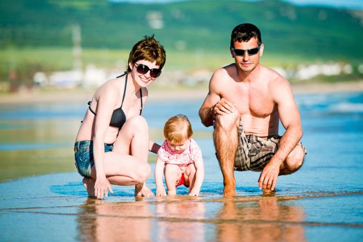Beautiful family with baby playing on the beach