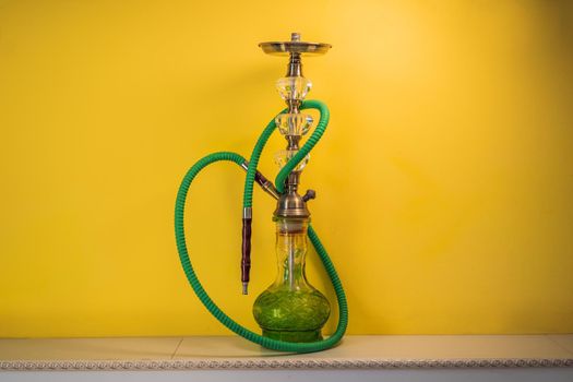 hookah shisha with glass flask and metal bowl with colored smoke on a yellow background. Traditional Eastern vacation for relaxation.