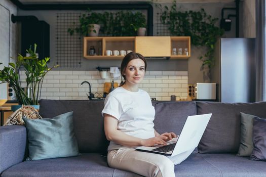 Portrait of pregnant woman at home, working remote with laptop online looking at camera and smiling