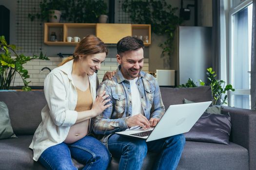 Online shopping. Young family, pregnant woman and man make an online purchase order from a laptop, holding a credit card. Sitting at home on the couch. Very happy, satisfied.