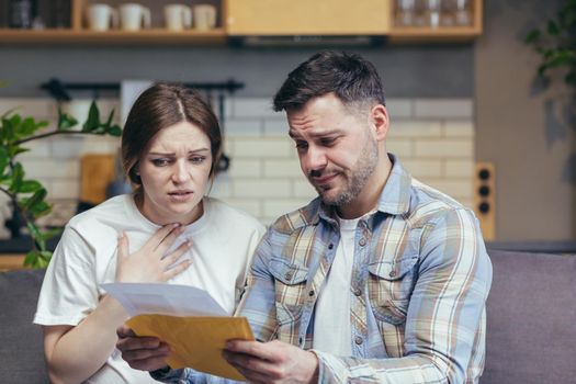 Disappointment. Young family. The man and the pregnant woman received a letter and documents. Bad news. Sitting at home on the couch