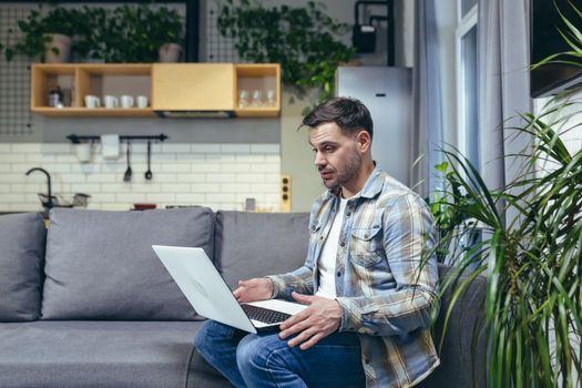 Young man working from home with laptop. Talks on video call. Sitting on the couch.