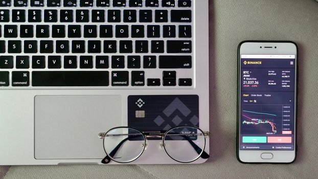 Laptop and phone to buy bitcoin on the Binance crypto exchange during the market crash. Trading, spot, staking. Workspace freelance flatlay