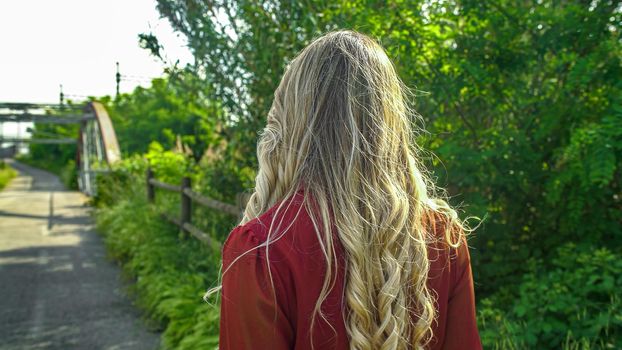 Back view of woman with beautiful long blond hair on the walking track of a park
