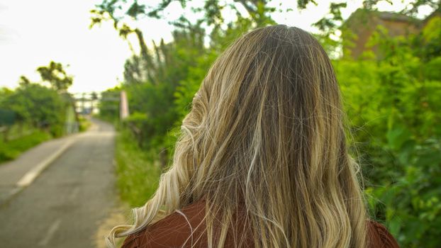 Back view of a girl walks in the park with beautiful long blond hair in daytime