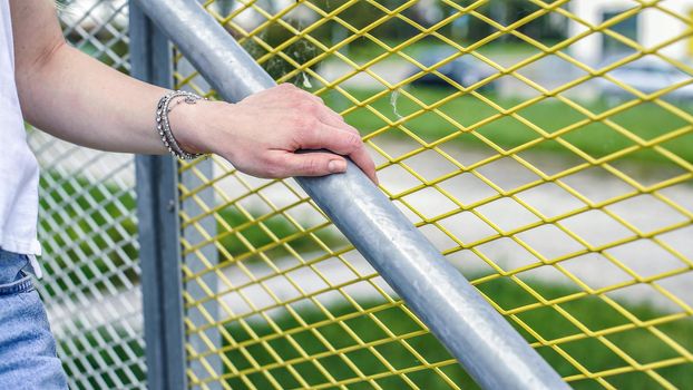 Girl comes downstairs holds onto handrail against net fence wearing a bracelet