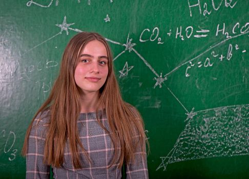 Student girl standing near clean blackboard in the classroom.