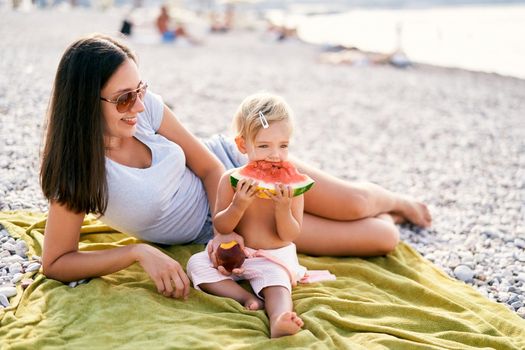 Mom holding out a peach to a little girl eating a watermelon. High quality photo