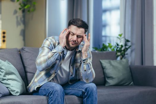 The sick man is sitting alone at home on the couch, has a severe headache