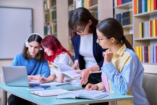 Group of teenage students study in school library classroom. Teen girl and female teacher mentor helping in their studies. High school, learning, education, knowledge, adolescence