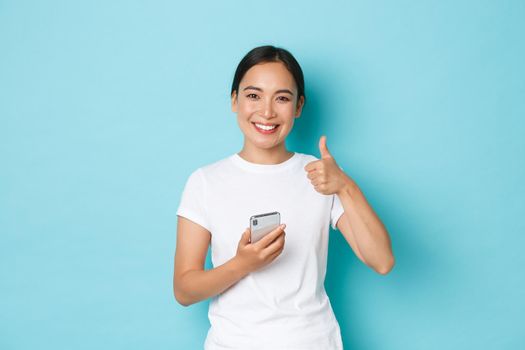 Lifestyle, technology and e-commerce concept. Satisfied beautiful asian female customer, client of online shop, leave positive feedback, holding smartphone and showing thumbs-up gesture.