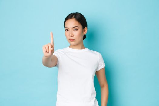 Serious-looking assertive young asian woman forbid action, express strong disapproval or disagree, shaking finger in warning sign, prohibit something bad, looking displeased and confident.