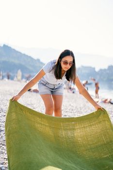 Young woman spreads a blanket on a pebble beach. High quality photo