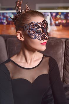 Portrait of a beautiful model wearing a crown and carnival mask in a black dress in the studio
