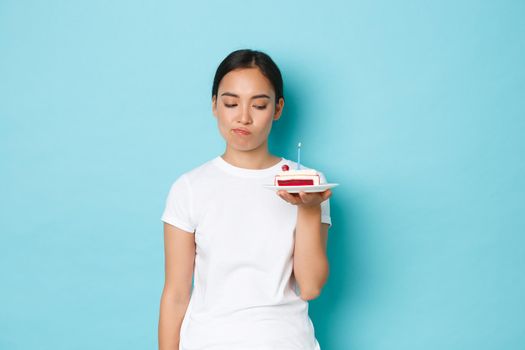 Holidays, lifestyle and celebration concept. Skeptical and disappointed asian girl in white t-shirt, complaining over bad birthday party, looking displeased at b-day cake with sulking expression.