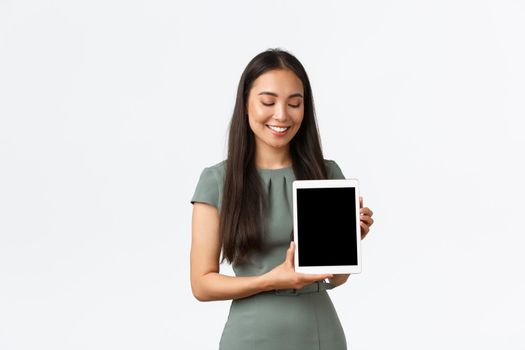 Small business owners, startup and work from home concept. Smiling asian female order product online, showing digital tablet screen with pleased expression, recommend application, white background.