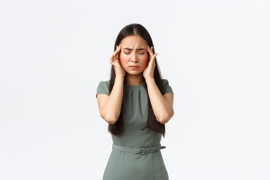 Small business owners, women entrepreneurs concept. Exhausted asian female in dress feeling sick, close eyes and touching temples, suffering painful headache, having migraine.