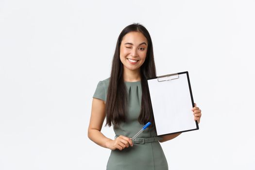 Successful smiling asian female entrepreneur showing clipboard with blank paper as if show-off her results, making survey or writing down clients info for small online store, manage own business.