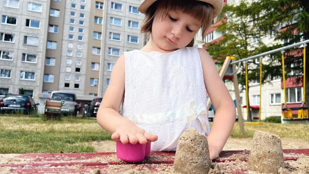 SMALL GIRL IN SUMMER DRESS playing with sand in the backyard of urban block houses in Tallinn, Estonia