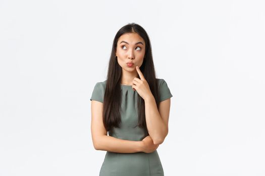 Small business owners, startup and work from home concept. Silly creative attractive asian woman thinking, pouting thoughtful and looking upper left corner dreamy, imaging something, white background.