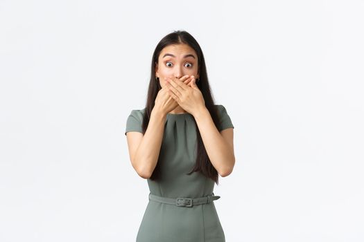 Small business owners, women entrepreneurs concept. Shocked and panicking asian woman slip secret, shut mouth and stare embarrassed, heard big rumor, standing white background.
