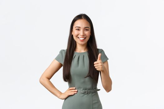 Small business owners, women entrepreneurs concept. Satisfied smiling asian female team leader praising great job, showing thumbs-up in approval, like result, white background.