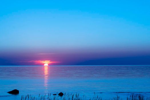 beautiful red sunset sun on the sea on the surface of the water. the bay, coastal rocks and the setting summer sun. seascape. sea resort