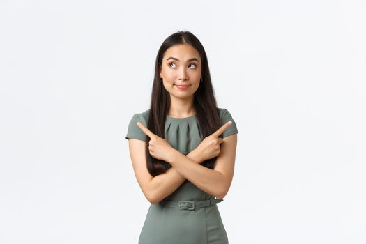Small business owners, women entrepreneurs concept. Indecisive cute asian woman trying make choice, shopping online, facing decision, pointing fingers sideways and look confused.