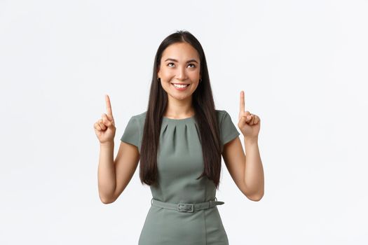 Small business owners, women entrepreneurs concept. Happy intrigued asian woman in dress pointing fingers up and looking tempting, want try something or buy at online store for special price.