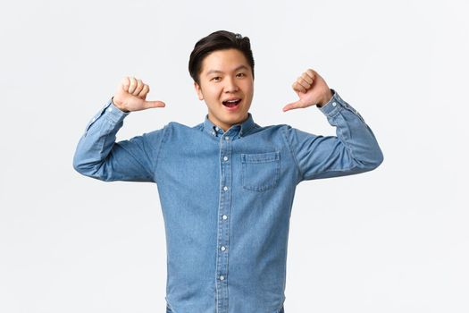 Proud and happy asian guy show-off, pointing at himself and smiling delighted, celebrate personal achievement, bragging, become champion, feeling success, standing white background.