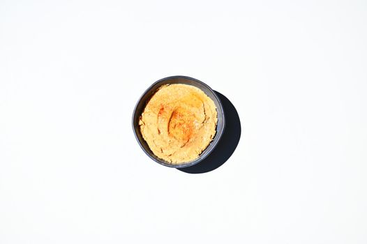 Flat lay. Top view. Food still life of traditional oriental meal- a chickpea hummus with sprinkled paprika peppers in blue ceramic bowl, isolated on white background with copy ad space for text