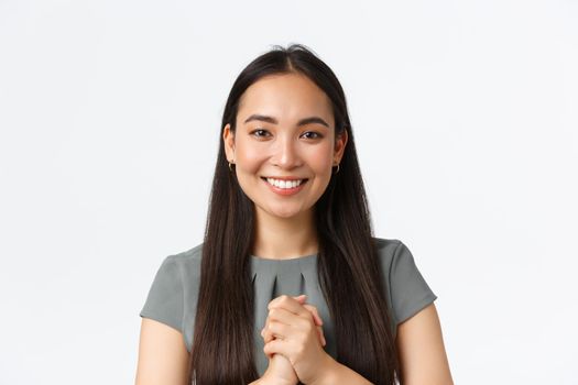 Close-up of happy attractive asian woman receiving award or praises at work, holding hands clasped together in thankful appreciation gesture, smiling, thanking for given opportunity, white background.