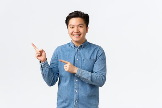 Smiling handsome asian male student showing project, making demonstration or announcement, pointing fingers upper left corner, recommend click link, online courses, white background.