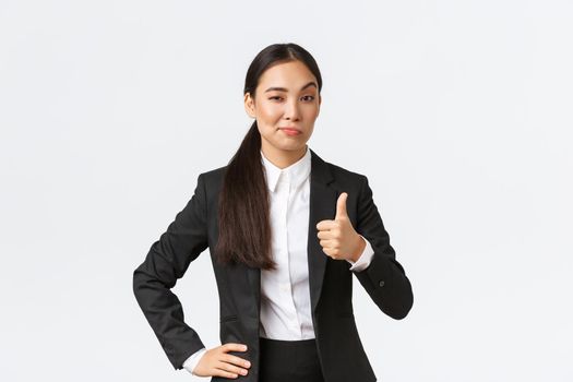 Pleased female entrepreneur, lady boss in black suit satisfied with your work, showing thumbs-up and nod in approval, praise great job, well done, standing white background.