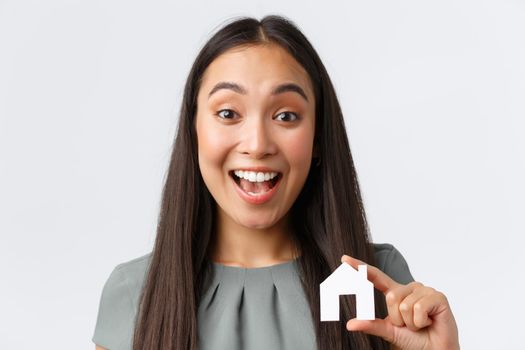 Insurance, loan, real estate and family concept. Excited smiling asian woman found perfect place to buy or rent, showing small house in hands and rejoicing, buying home, standing white background.