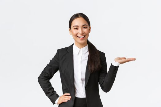 Professional smiling businesswoman introduce her project during meeting. Saleswoman in black suit holding hand right as showing product, holding on palm over blank white background.