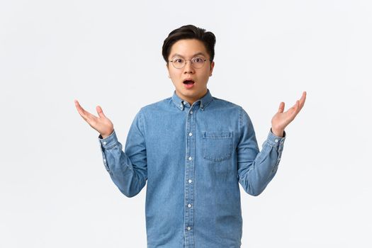 Surprised and confused asian man in braces and glasses cant understand how this happened, raise hands up and shrugging startled and puzzled, dont know, standing amazed white background.